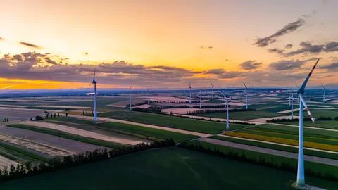 Wind farm across strip fields under sunset clouds. Towers extend toward the.. Stock Photos
