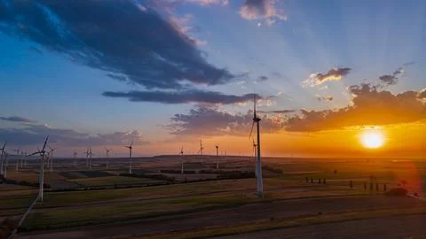 Wind farm beneath a cloud bank beside the setting sun. A tower stands near .. Stock Photos