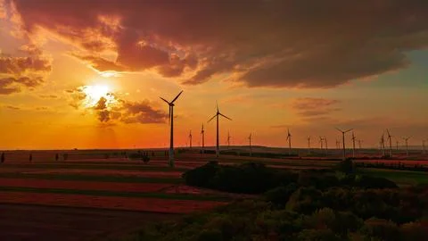 Wind farm beneath orange clouds at sunset. A tower stands to the right of t.. Stock Photos