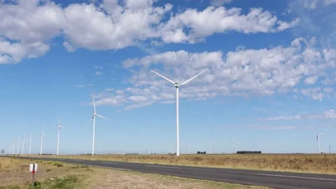 Wind farm in a field next to a road. Windmills turning slowly, Blue sky with Stock Footage 171385401