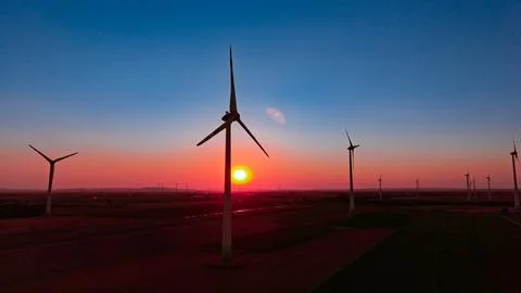 Wind farm under gradient sky at dusk. Multiple generators stand on agricult.. Stock Photos