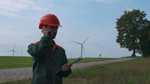 Wind farms in the field, rotating blades. Engineer is talking on the phone. Stock Footage