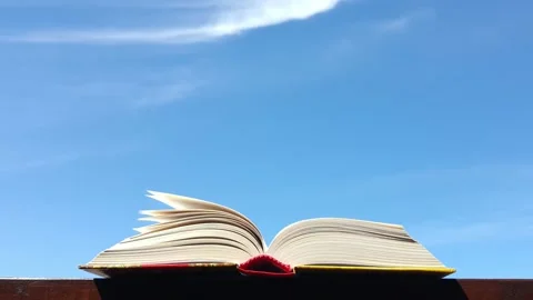 The wind flips through the pages of the book against the blue sky Видео 156047428