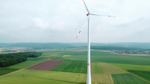 The wind generator stands on a green field, villages can be seen in the distance Stock Footage 155595424