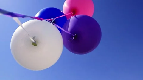 The wind plays with a group of balloons against a beautiful green meadow on blue Video stock 134516926