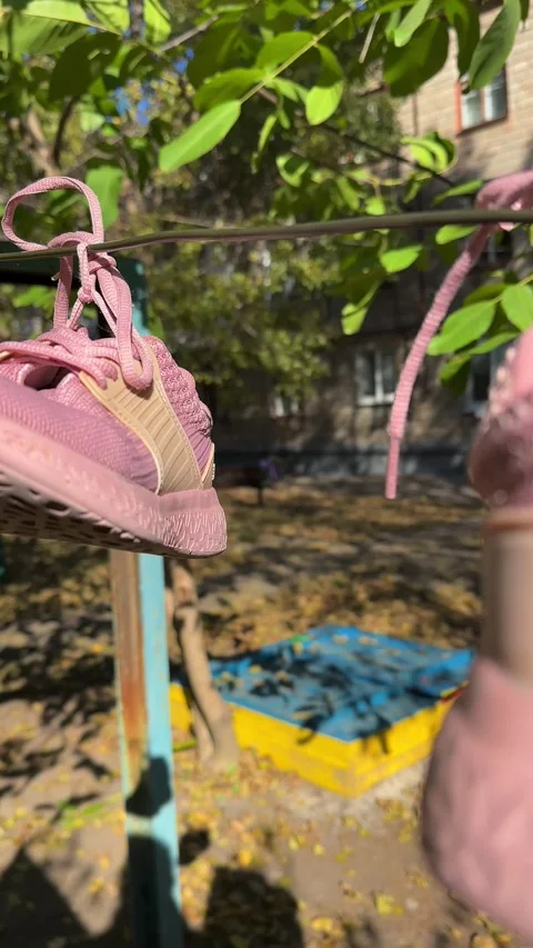 The wind rocks pink sneakers that dry on a rope. A child is running in the Stock Footage 253884892