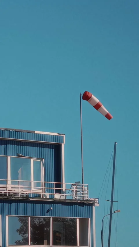 Wind sock on a tall pole sways gently in the breeze above a blue building with 库存影片 329201820