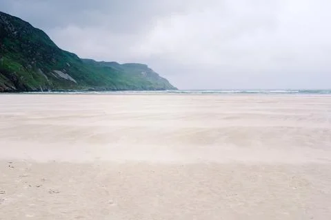 Wind sweeps sand across a pristine beach in Ireland under a moody sky with .. Stock Photos