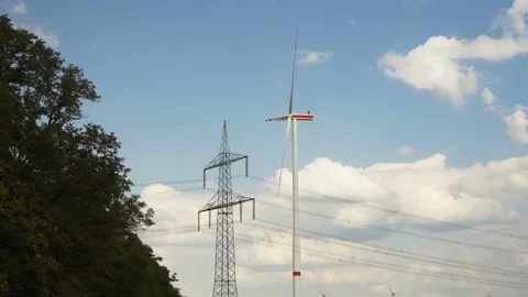 Wind turbine and high voltage tower next to tree from low angle Stock Footage 203908917