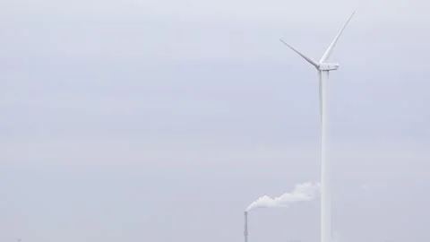 Wind turbine and smoke stack in countryside symbolize green tech and industrial Stock Footage 277509984