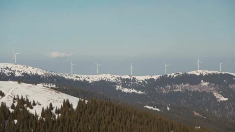 Wind turbine array on distant snowy mountain ridge above pine forest Stock-Footage 331961056