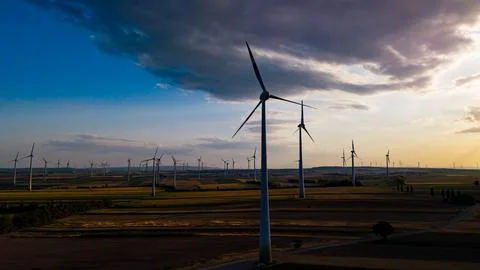 Wind turbine beneath a gray cloud over farmland. A white tower fills the fo.. Stock Photos