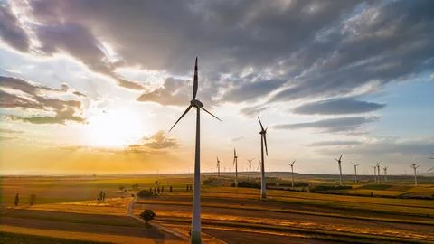 Wind turbine beneath a gray cloud at golden hour. The sun lights the left h.. Stock Photos