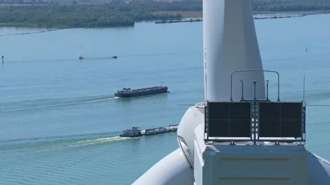 Wind turbine blade passing over cargo ships navigating river 動画素材 345027240