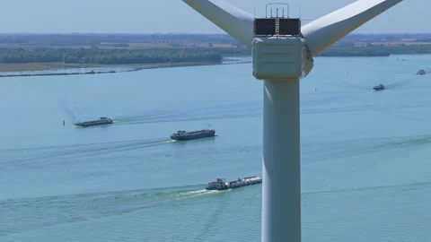 Wind turbine blades rotating with barges navigating a river Видео 345026686