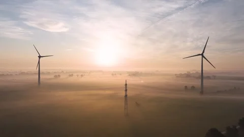 Wind turbine casting long shadows over misty field at sunrise Stock Footage 288239188