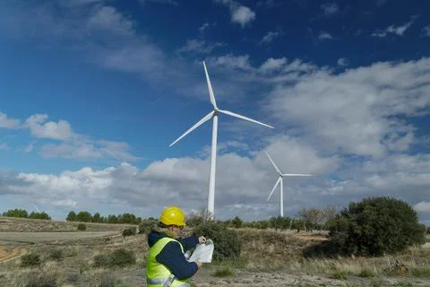 Wind turbine engineer inspecting blueprints in a wind farm with cloudy sky Stock Photos