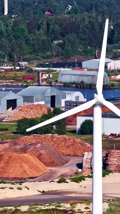 Wind turbine rises above a timber processing site, highlighting renewable Stock Footage 341385619