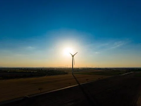 A wind turbine rises high in the middle of a field as the sun sets. The sky s Stock-Fotos