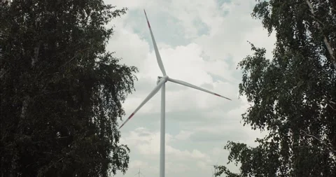 Wind turbine rotating between green trees under cloudy sky Stock Footage 305014117