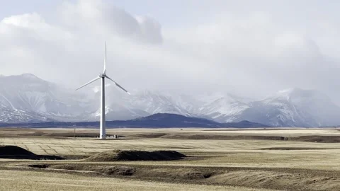 Wind turbine rotating on open landscape with mountains in background. Stock Footage 329129608