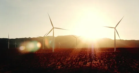 Wind turbine spinning at sunset in desert with lens flare creating clean energy Stock Footage