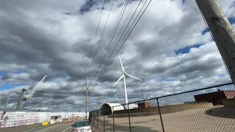 Wind Turbine Spins Under Cloudy Sky at Industrial Site Stock Footage 317632439