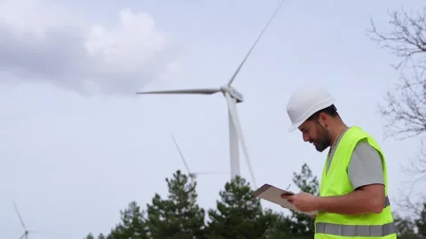 A wind turbine technician thoughtfully examines a clipboard, wearing a hard h Stock-Footage 276312477