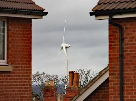 A wind turbine visible between two houses. The turbine is situated by the sid Stock-Fotos