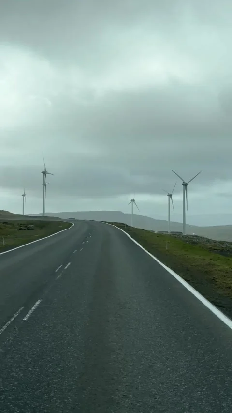 Wind turbines along a roadside seen from a moving car , Faroe Islands 스톡 동영상 334869243