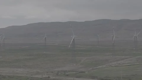 Wind Turbines in Arid Landscape with Mountain Backdrop on Overcast Day Stock Footage 341970435