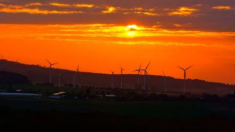Wind Turbines at Dramatic Orange Sunset Over Green Fields Foto stock