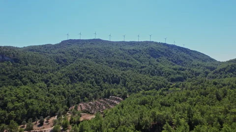 Wind turbines on a forested mountain during clear blue skies Video stock 290091937