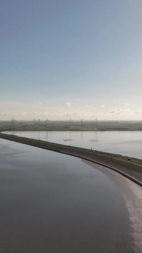 Wind turbines generating renewable energy along a coastal causeway Stock Footage 327113756