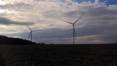 Wind turbines generating renewable energy in green field at cloudy sunset Stock Footage 341130058