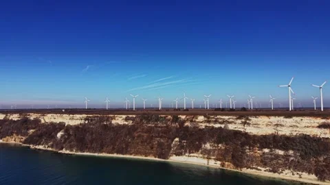 Wind turbines line the coastline under a clear blue sky near the water Stock Footage 336542108