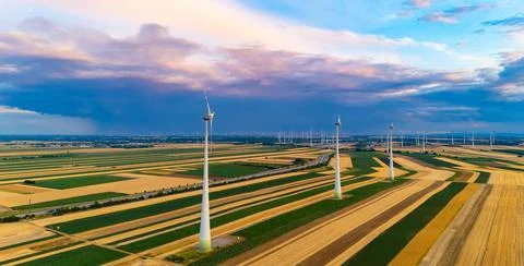 Wind turbines over patterned fields beneath storm clouds. Drone view with f.. Stock Photos