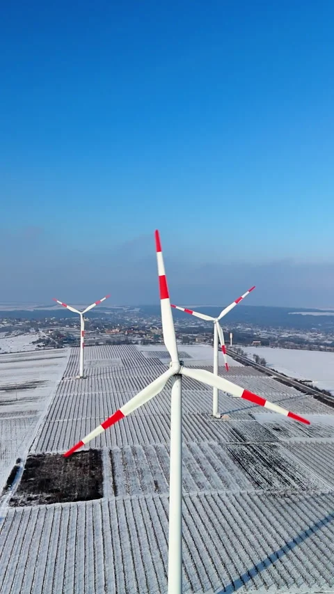 Wind turbines with red and white blades rotate against a clear blue sky above a Stock Footage 340274732