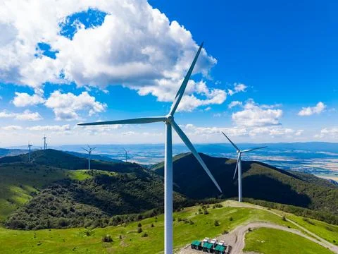 Wind turbines rotate on hills while some clouds float overhead. Green fields  Foto stock