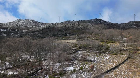 Wind Turbines Rotating on Snow-Dusted Rocky Hillside Above Bare Winter Forest Video stock 327663582