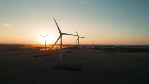 Wind turbines silhouetted by the setting sun over fields of golden crops, a Stock Footage 288316088