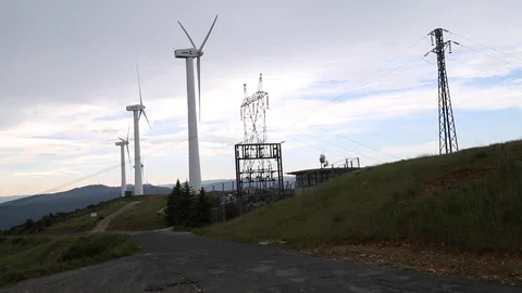 Wind turbines spin alongside power station and power lines Stock Footage 123979710