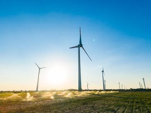 Wind turbines spin in the breeze while large sprinklers water the fields in t Stock Photos