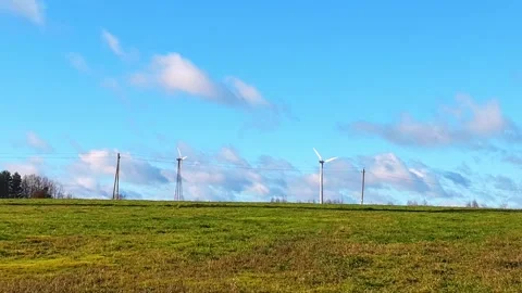 Wind turbines spin in clear sky over green field on sunny day in rural area Stock Footage 325041434