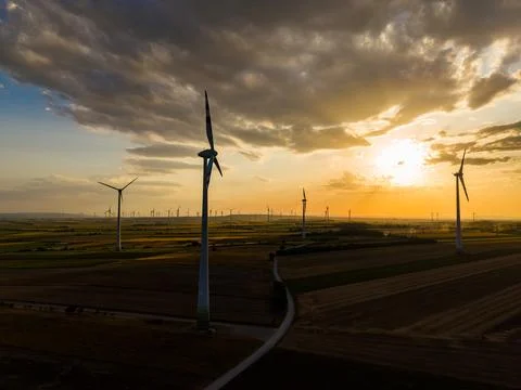 Wind turbines spin gently in a vast field during the evening hours as the sun Stock-Fotos