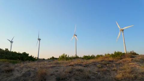 Wind turbines spin gracefully under clear skies in a serene landscape at suns Stock Footage 313628220