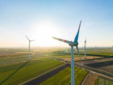 Wind turbines spin in a large open field as the sun sets, casting a warm glow Stock Photos