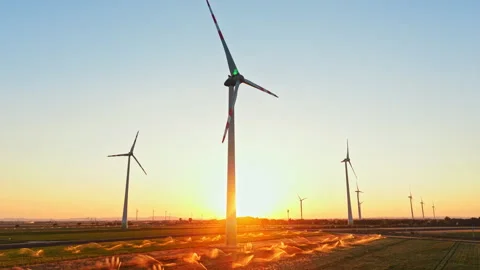 Wind turbines spin as sun rises over a field at dawn in an open landscape near a Stock Footage 344264152
