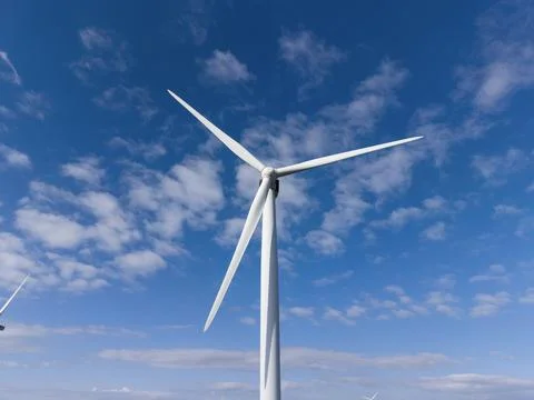 Wind turbines spin under a blue sky with clouds in the background Stock Photos