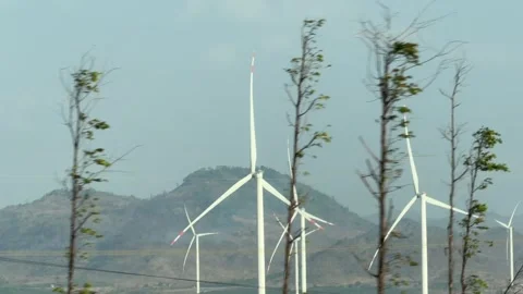 Wind turbines stand across an open field viewed from a moving car while passing Stock Footage 336318404